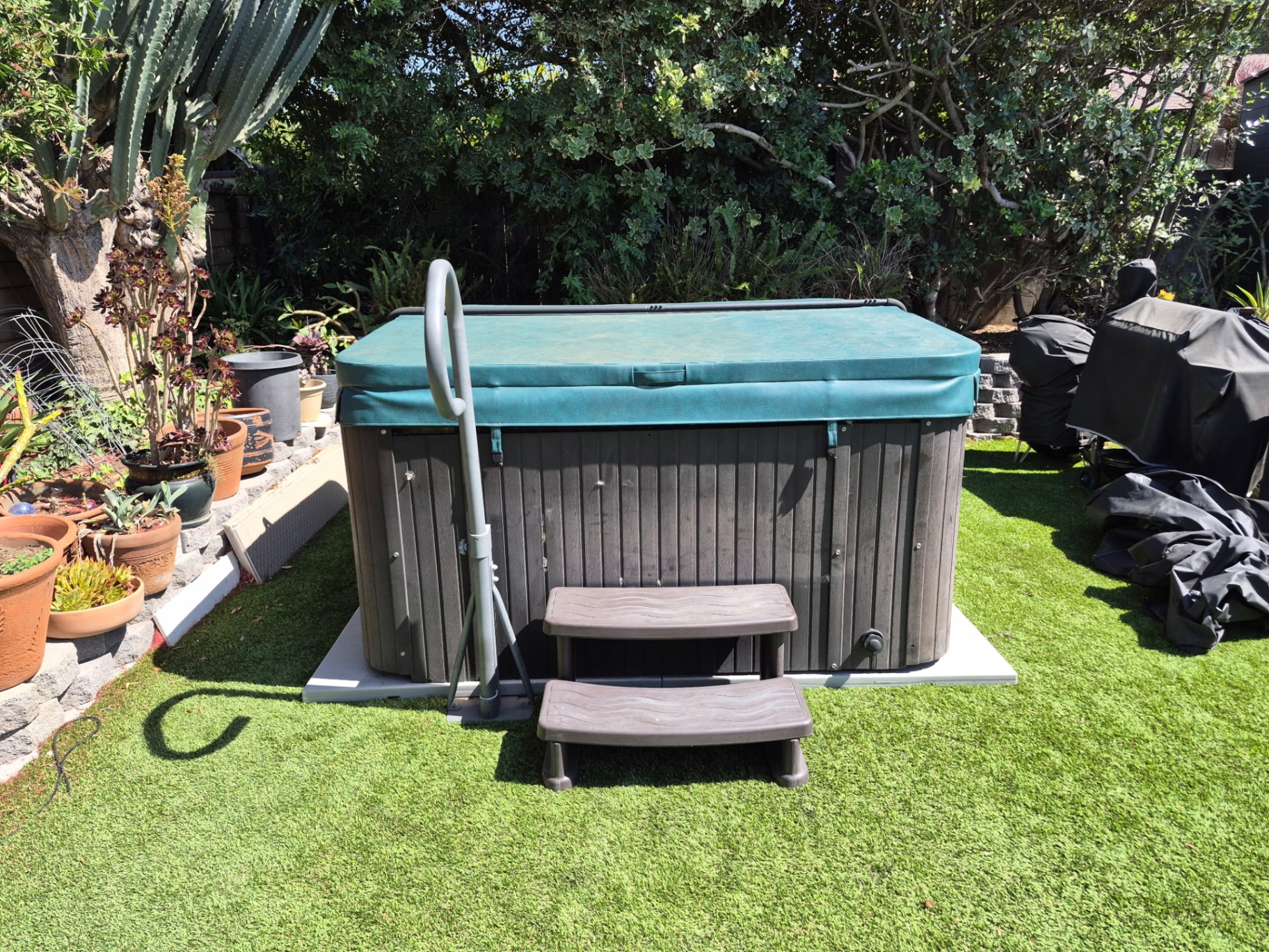 Hot tub set on turf with teal cover in a Claremont backyard after relocation